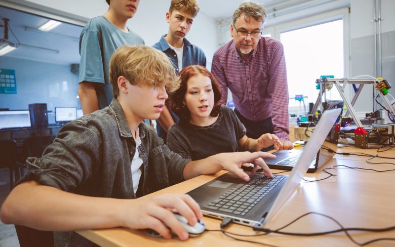 Group of Gen Z teenage high school students and male teacher, using laptop durning programming lessons.